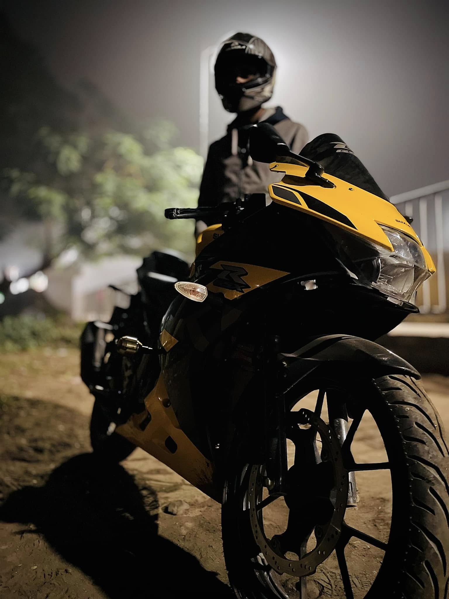 A man with a helmet stands next to a yellow and black sports bike at night.