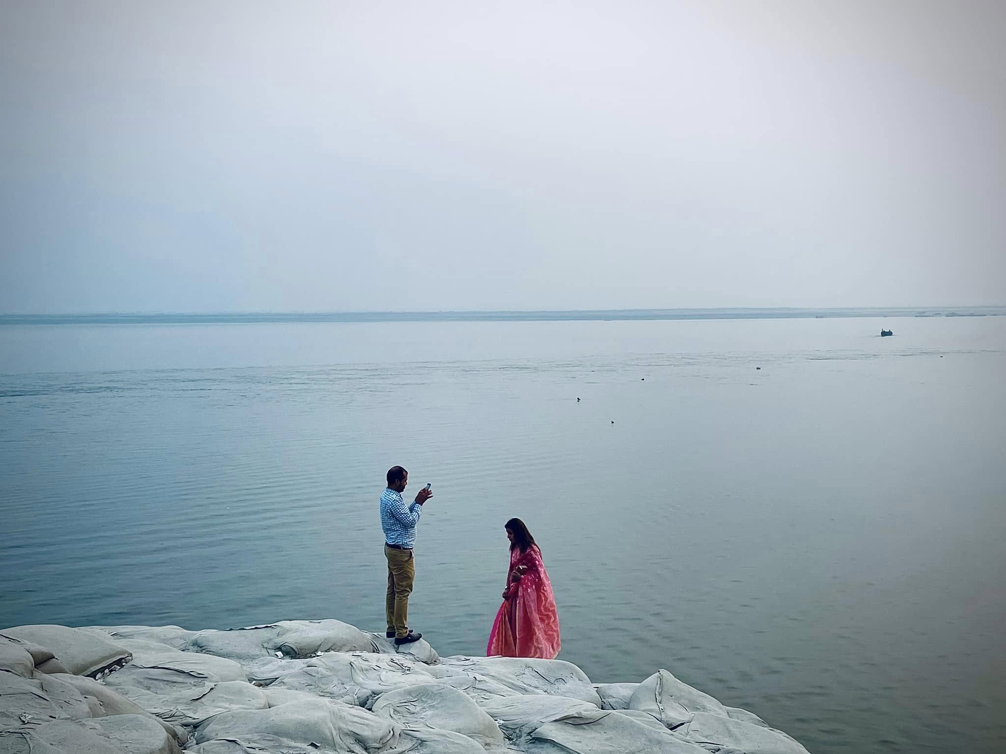 A couple standing on sandbags near a wide river on a foggy day.