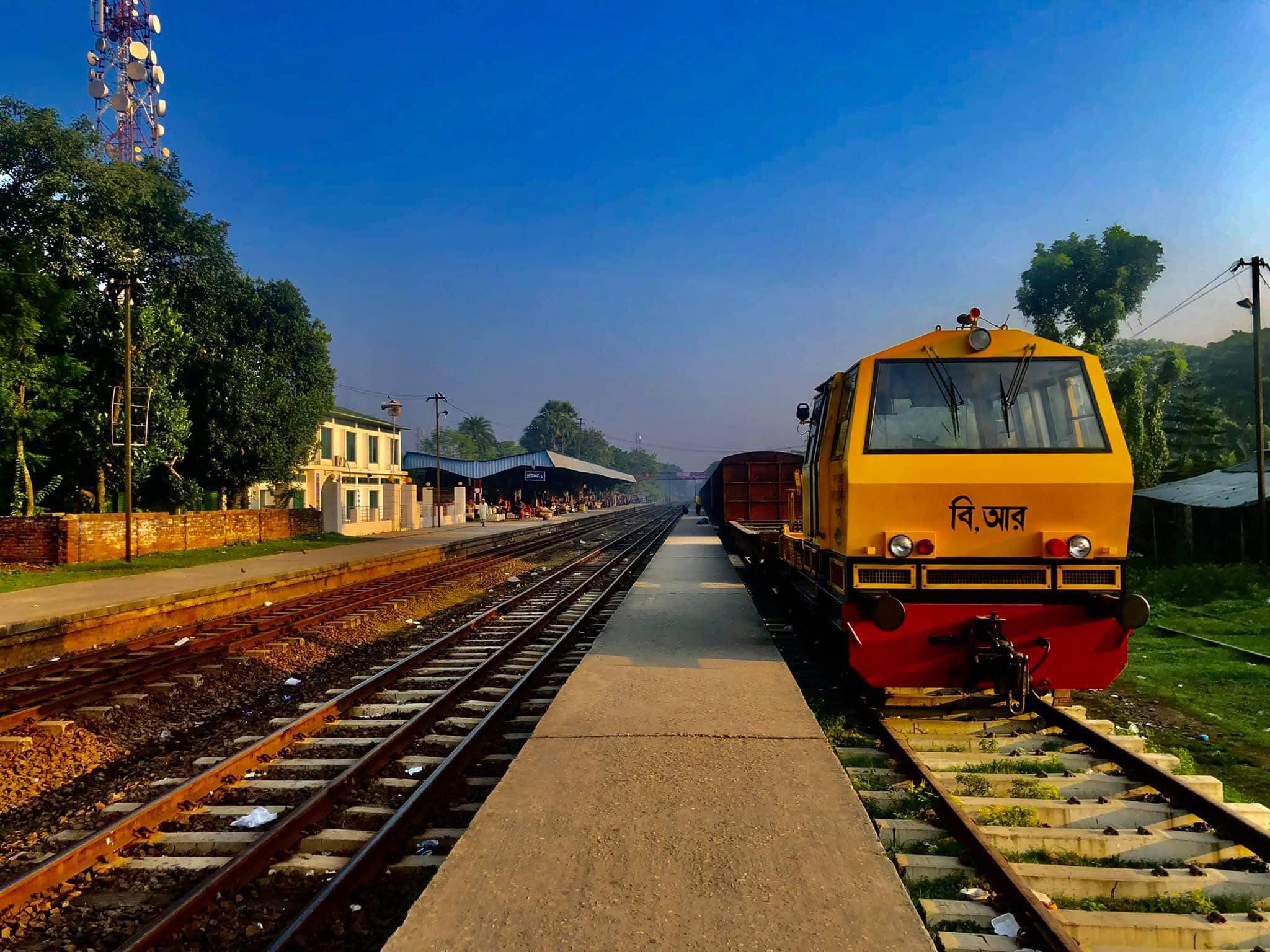 A yellow diesel locomotive at a railway station under a bright blue sky.