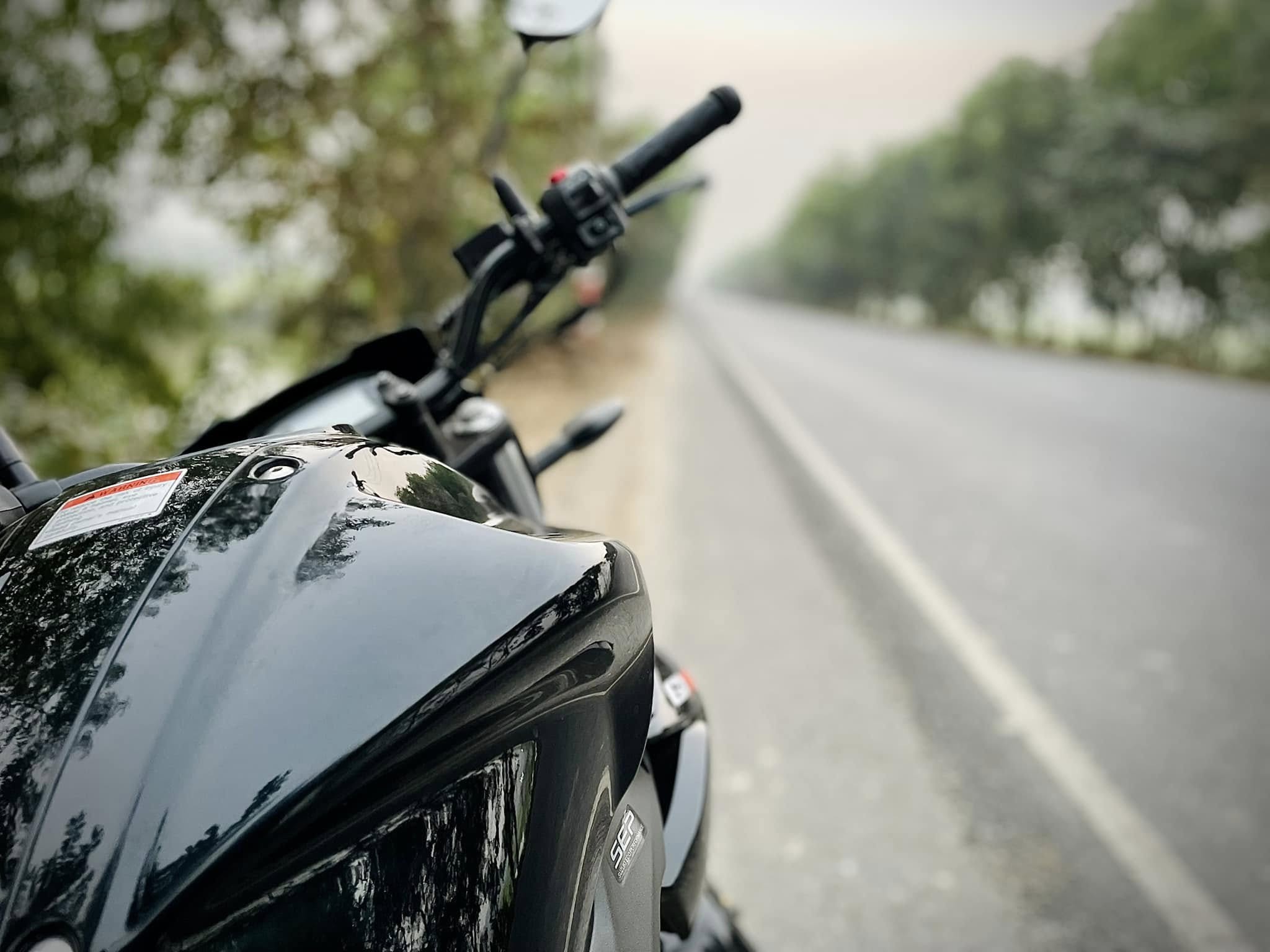 Close-up of a black motorcycle on the side of a highway on a foggy day.